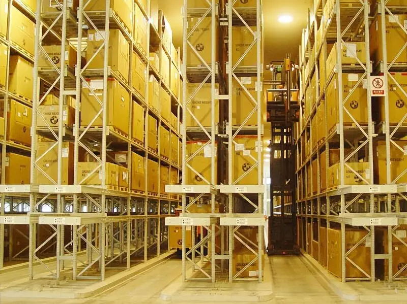 Specialized guided very narrow aisle forklift operating in narrow channel, storing pallets at high level.